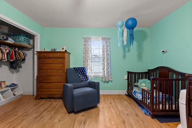 bedroom featuring a nursery area, a closet, baseboards, and wood finished floors