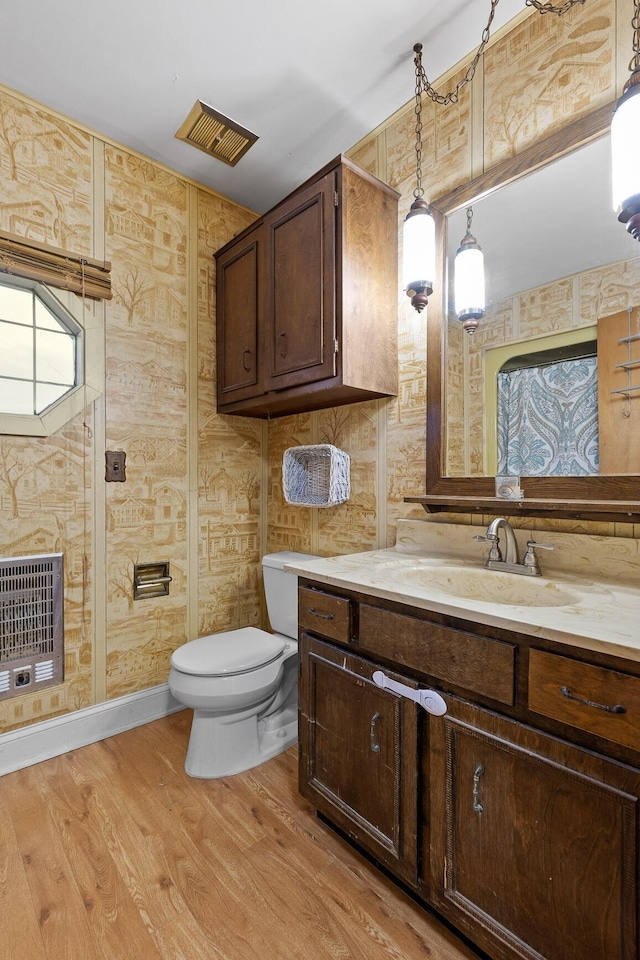 bathroom featuring heating unit, toilet, vanity, wood finished floors, and baseboards