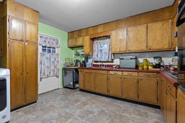 kitchen featuring washer / dryer, brown cabinetry, a sink, and a textured ceiling