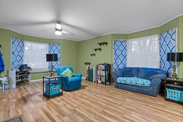 living area featuring a textured ceiling, wood finished floors, a ceiling fan, and crown molding