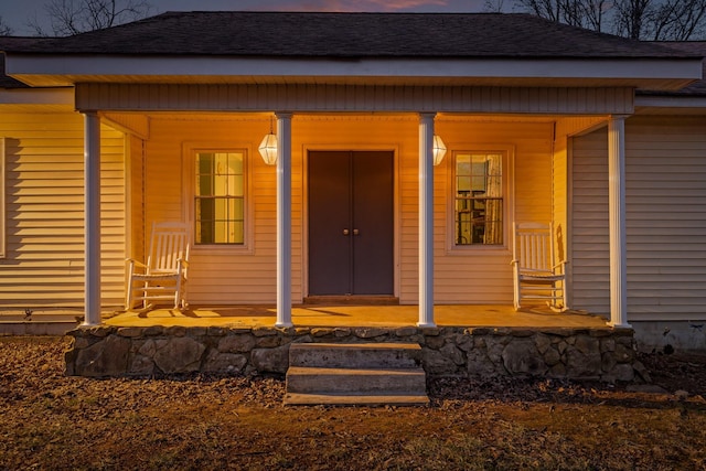 exterior entry at dusk featuring a porch and a shingled roof