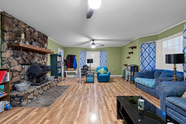 living room with a ceiling fan, a wood stove, a textured ceiling, and wood finished floors