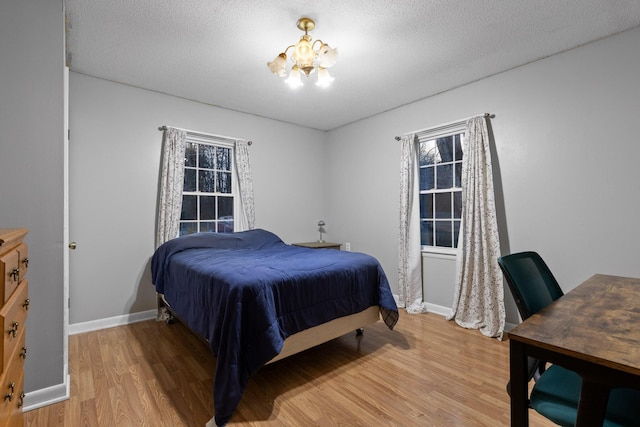 bedroom with light wood finished floors, baseboards, a textured ceiling, and an inviting chandelier