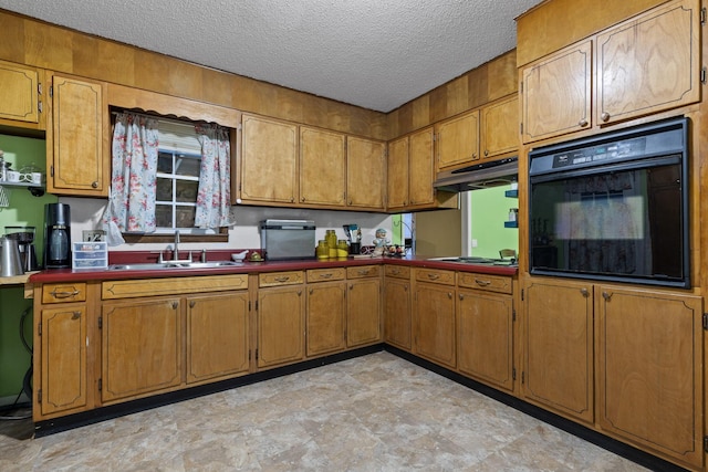 kitchen with brown cabinetry, a sink, black oven, stovetop, and under cabinet range hood