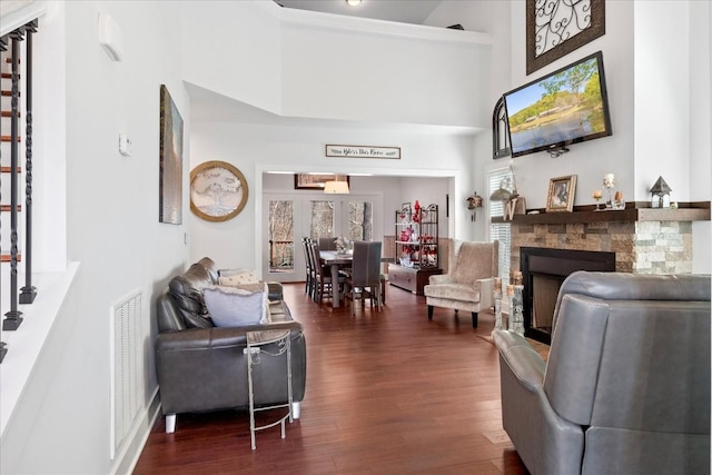 living room featuring visible vents, a stone fireplace, dark wood-type flooring, and a high ceiling