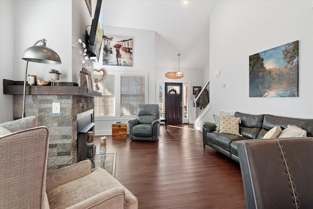 living room with stairway, baseboards, high vaulted ceiling, a stone fireplace, and dark wood-type flooring