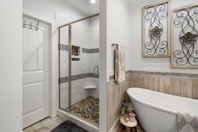 full bathroom featuring a wainscoted wall, tile walls, a stall shower, and a freestanding bath