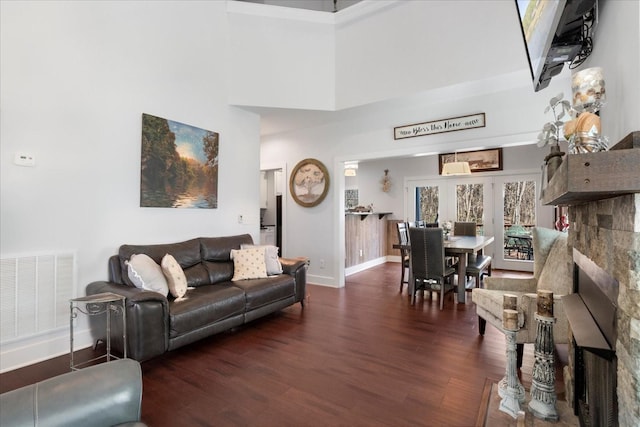 living room with visible vents, baseboards, wood finished floors, and a towering ceiling