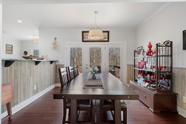 dining space with wood walls, crown molding, baseboards, and wood finished floors