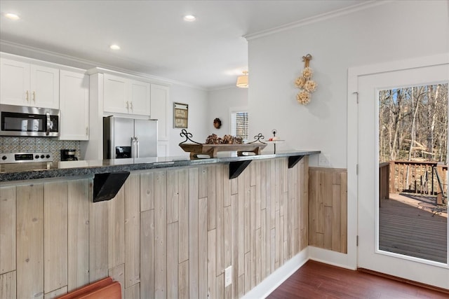 kitchen featuring dark countertops, appliances with stainless steel finishes, a breakfast bar, and crown molding