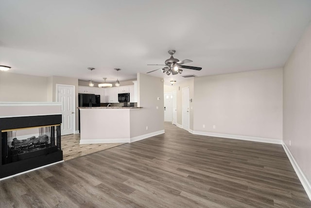 unfurnished living room featuring ceiling fan, baseboards, wood finished floors, and a multi sided fireplace