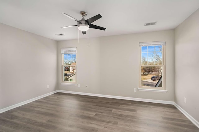 spare room with dark wood-type flooring, a ceiling fan, visible vents, and baseboards