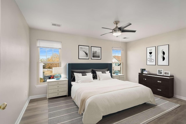 bedroom with a ceiling fan, visible vents, baseboards, and wood finished floors