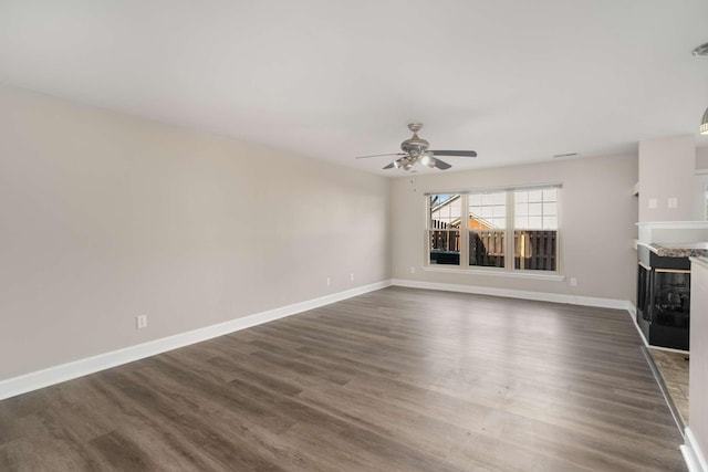 unfurnished living room featuring ceiling fan, dark wood-style flooring, a high end fireplace, and baseboards