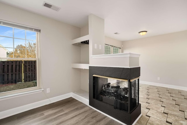 unfurnished living room with baseboards, visible vents, wood finished floors, and a multi sided fireplace