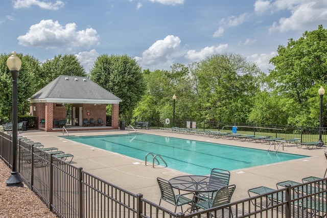 community pool with fence, an outdoor structure, and a patio