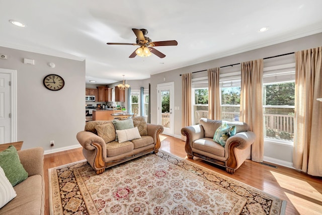 living area with ceiling fan with notable chandelier, light wood finished floors, crown molding, and baseboards