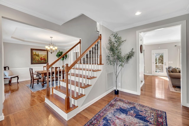stairway with a chandelier, wood finished floors, visible vents, baseboards, and ornamental molding