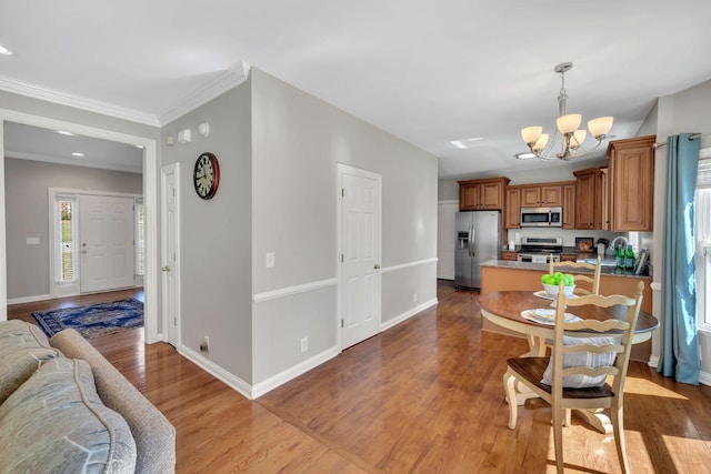 kitchen with baseboards, appliances with stainless steel finishes, brown cabinets, wood finished floors, and a notable chandelier
