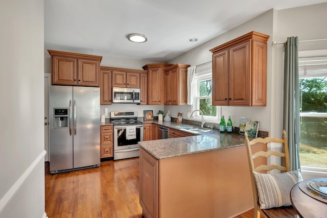 kitchen with stainless steel appliances, stone countertops, brown cabinetry, a sink, and a peninsula