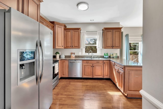 kitchen featuring light wood finished floors, appliances with stainless steel finishes, stone countertops, a sink, and a peninsula