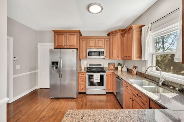 kitchen with baseboards, appliances with stainless steel finishes, wood finished floors, light stone countertops, and a sink