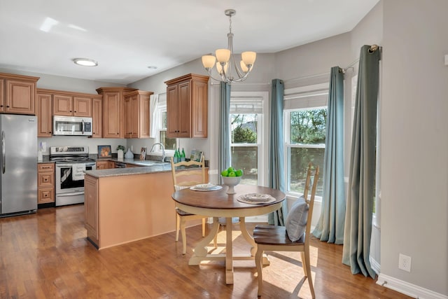kitchen with a chandelier, stainless steel appliances, a peninsula, a sink, and wood finished floors