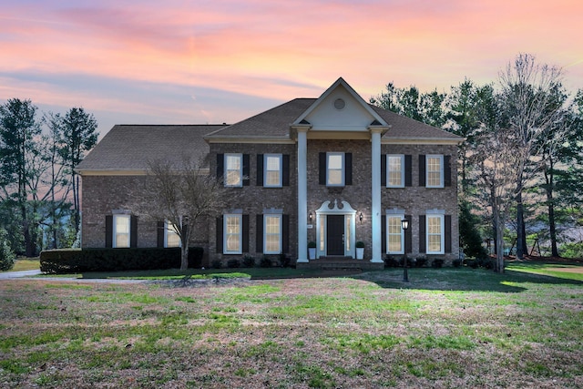 greek revival house featuring a lawn and brick siding