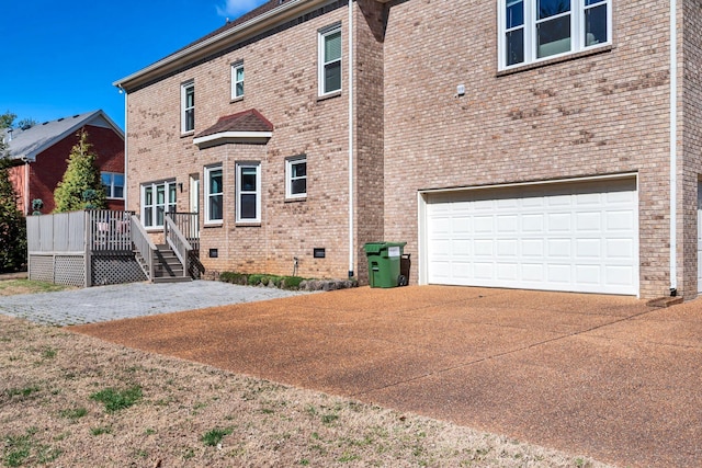 back of property featuring a garage, driveway, brick siding, and a wooden deck