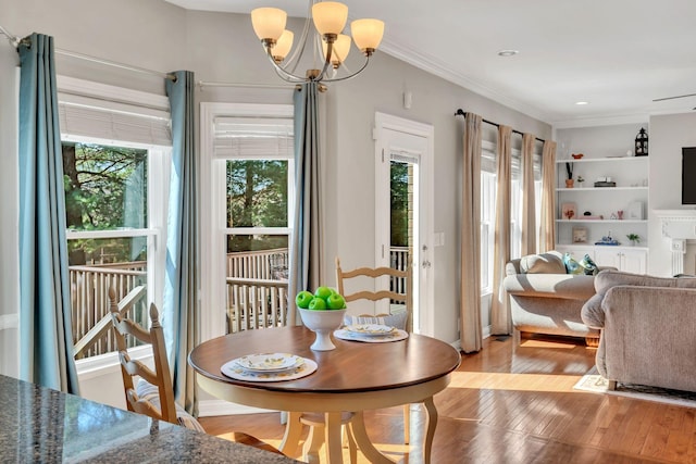 dining area with a notable chandelier, built in shelves, crown molding, and light wood-style floors