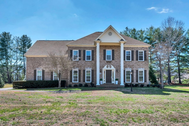 neoclassical / greek revival house featuring brick siding, a front lawn, and roof with shingles