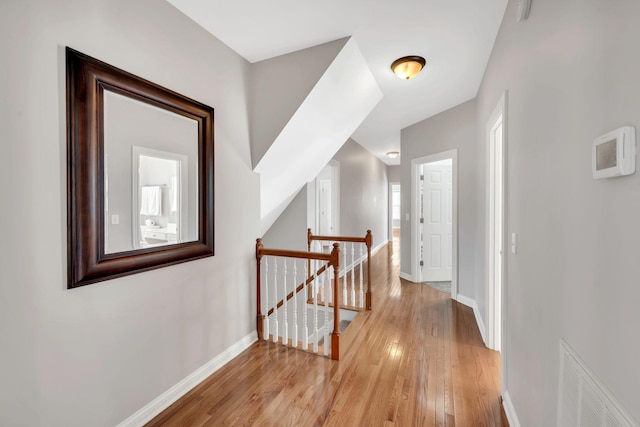 corridor featuring visible vents, light wood-type flooring, an upstairs landing, and baseboards