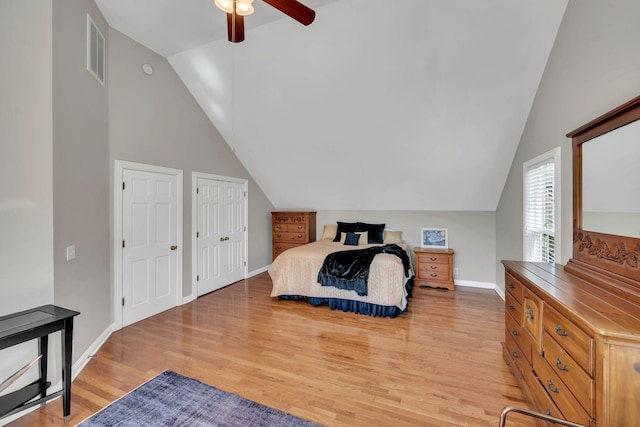 bedroom with visible vents, baseboards, vaulted ceiling, light wood-type flooring, and two closets