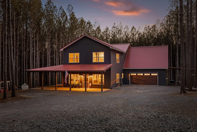 view of front of house featuring gravel driveway, an attached garage, a porch, and metal roof