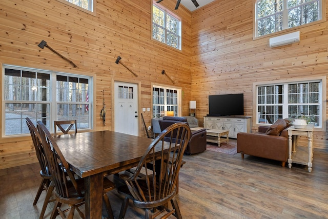 dining space with a wall unit AC, wood walls, and wood finished floors