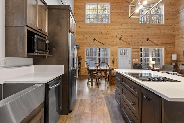 kitchen featuring black electric cooktop, dark brown cabinetry, a high ceiling, wood walls, and light countertops