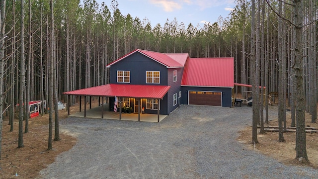 view of front of property with gravel driveway, metal roof, and a view of trees