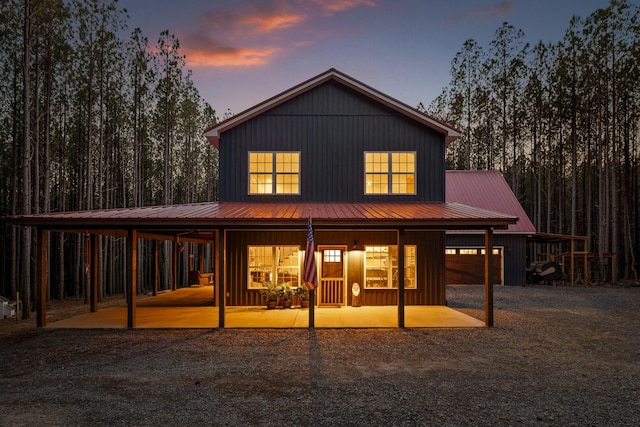 back of house at dusk with dirt driveway, metal roof, and board and batten siding