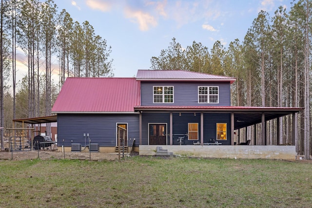 rear view of property featuring cooling unit, metal roof, and a lawn