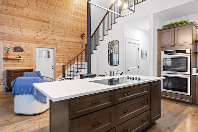 kitchen with wooden walls, wood finished floors, black electric stovetop, light countertops, and stainless steel double oven