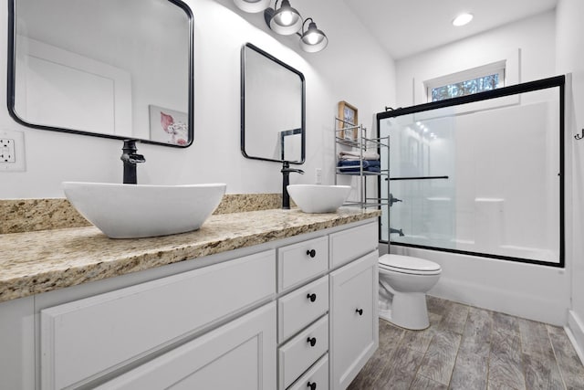 full bath featuring double vanity, combined bath / shower with glass door, a sink, and wood finished floors