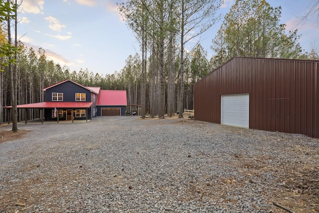 exterior space with a garage, gravel driveway, metal roof, and an outdoor structure