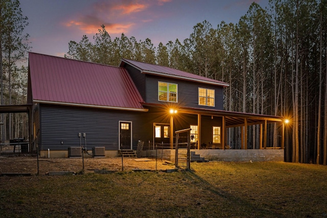 back of property at dusk with central air condition unit, metal roof, an attached carport, and a yard