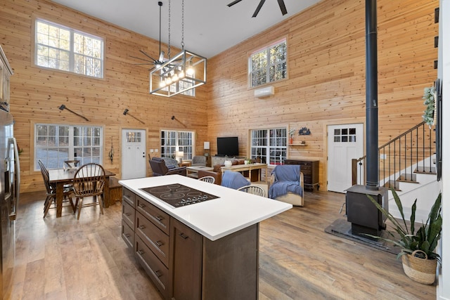 kitchen with light wood finished floors, ceiling fan, a wood stove, black electric stovetop, and wood walls