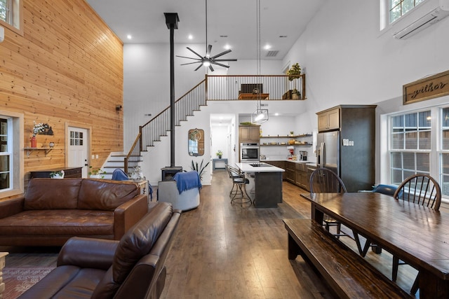 living area featuring a wall unit AC, ceiling fan, stairway, hardwood / wood-style floors, and wood walls