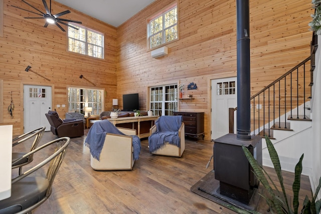 living area featuring wooden walls, ceiling fan, wood finished floors, a wood stove, and a healthy amount of sunlight