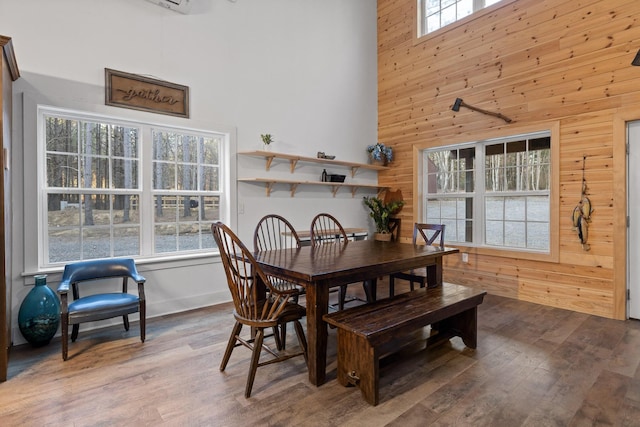 dining space with a healthy amount of sunlight, wood walls, a towering ceiling, and wood finished floors