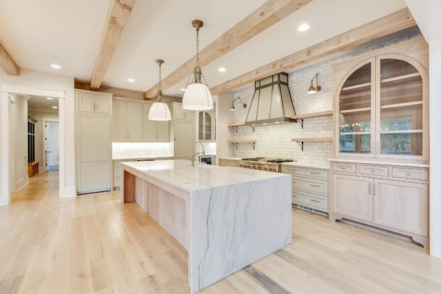 kitchen with light wood finished floors, beam ceiling, stainless steel gas stovetop, a large island, and wall chimney exhaust hood