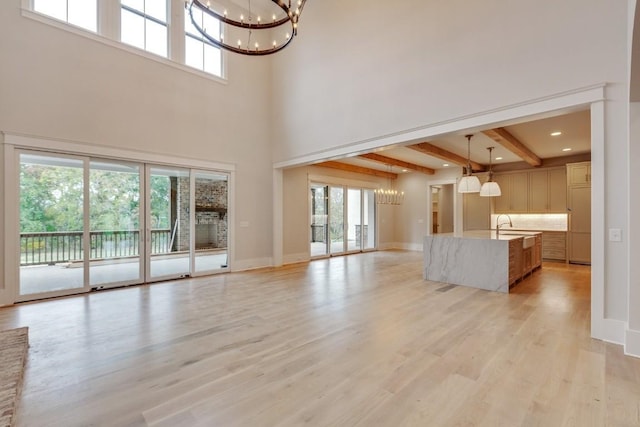 unfurnished living room with light wood-style floors, baseboards, a notable chandelier, and beamed ceiling