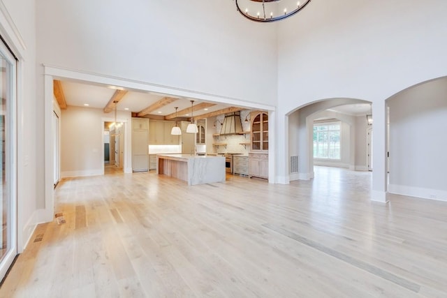 unfurnished living room featuring arched walkways, an inviting chandelier, a towering ceiling, and light wood finished floors